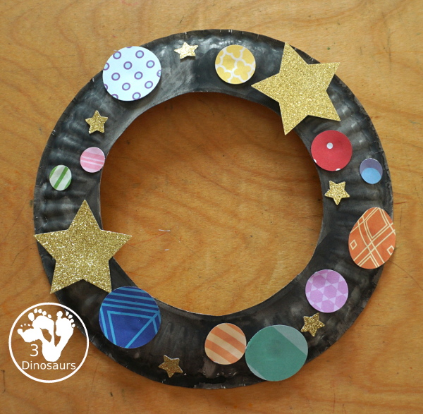 Scrapbook Paper Space Wreath Craft - a fun space craft for kids that is made with a paper plate, craft punches that are circles and stars with glitter paper and scrapbook paper. It makes a fun space craft. - 3Dinosaurs.com