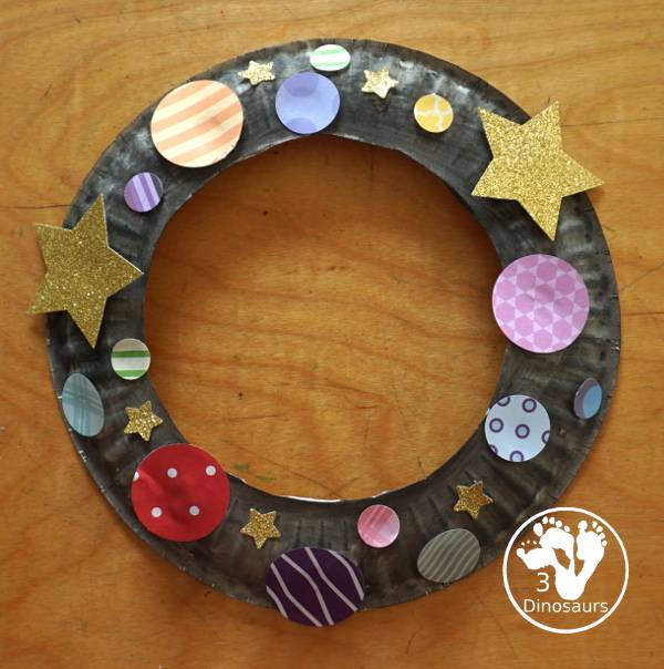 Scrapbook Paper Space Wreath Craft - a fun space craft for kids that is made with a paper plate, craft punches that are circles and stars with glitter paper and scrapbook paper. It makes a fun space craft. - 3Dinosaurs.com